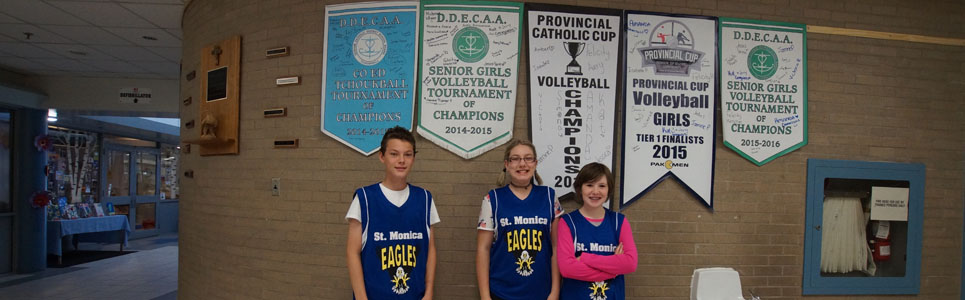 Three St. Monica Catholic School athletes in front of several sports banners on the wall.